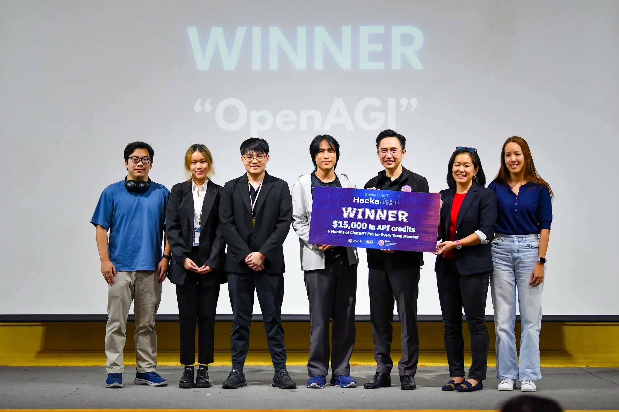 Buta and the OpenAGI team holding the OpenAI × AIAT Hackathon WINNER board on stage